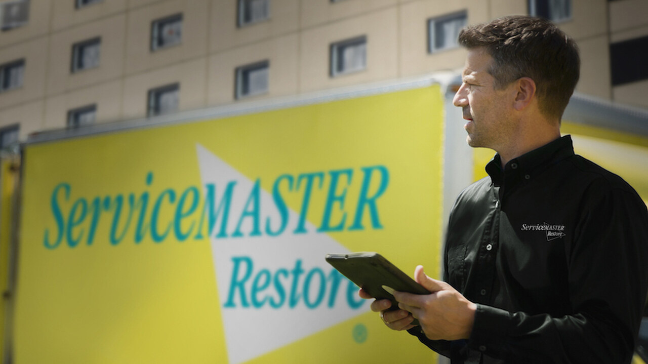 ServiceMaster Restore commercial technician with tablet in front of a branded ServiceMaster Restore box truck outside a multi-story building